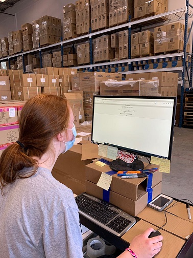 An employee works on a PPE shipment, facing a wall of health care supplies